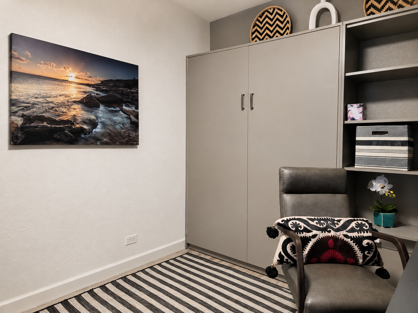 Modern coastal guest room featuring a custom Murphy bed with integrated shelving, built-in desk, striped area rug, and multifunctional workspace in a beach condo